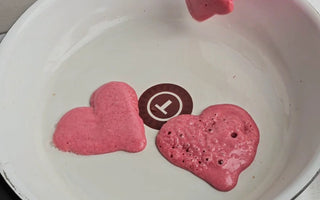 Pink heart-shaped pancakes cooking in white pan with spatula, perfect for mess-free family meals