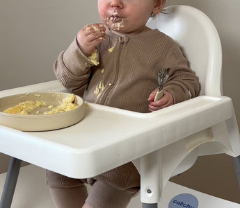 Baby eating messy meal in high chair with Catchy floor mat protecting flooring from food spills